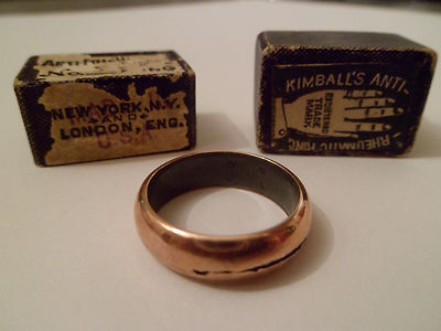 A plain metal ring similar to a wedding band. The box in which it originally came is also pictured; this now quite battered but it shows the company tradmark of a hand.